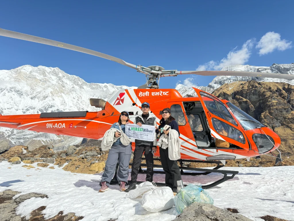 Helicopter landing at Annapurna Base Camp with tourists holding Everest Hikes banner in the Himalayas.