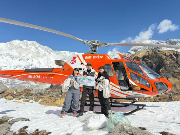 Helicopter landing at Annapurna Base Camp with tourists holding Everest Hikes banner in the Himalayas.