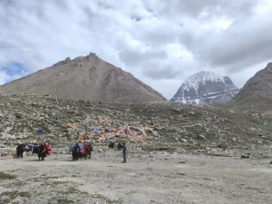 Pilgrims carrying goods with yaks and colorful prayer flags along the rocky high Himalayan trail towards Mount Kailash.