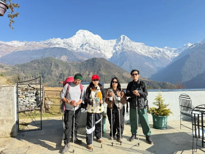 Four trekkers are carrying backpacks and enjoying the beautiful experience of Annapurna South in the sunshine.