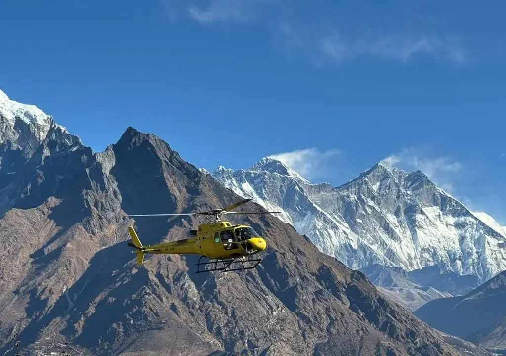 helicopter flying from Gorakshep to Lukla with Mount Everest and neighboring Himalayan peaks in the background under a clear blue sky.”