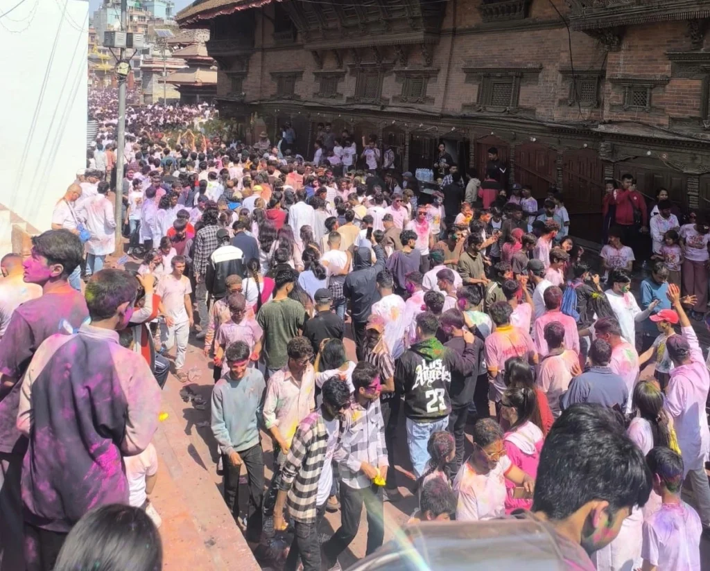 Large crowd celebrating Holi festival in Kathmandu Durbar Square, playing with colors and enjoying the vibrant street celebration.