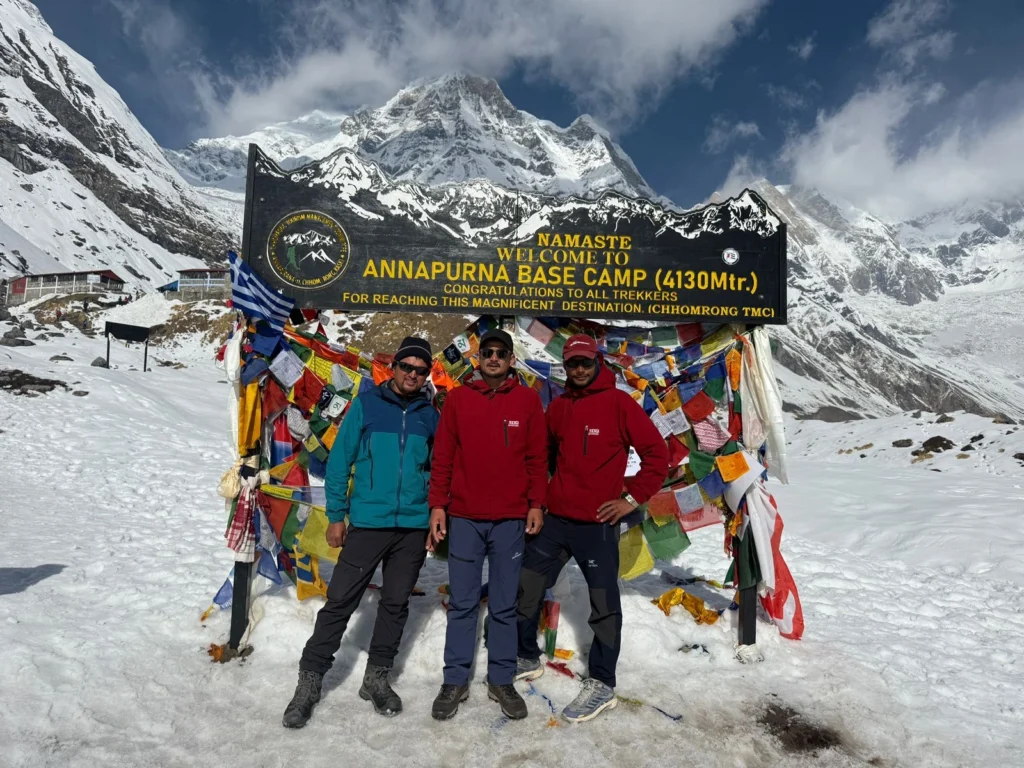 Three trekkers in front of the Annapurna Base Camp welcome sign.