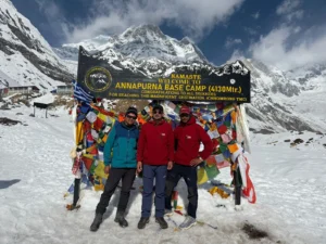 Three trekkers in front of the Annapurna Base Camp welcome sign.