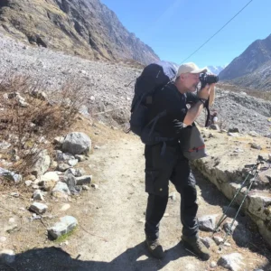 How to Trek Langtang Valley as a Beginner: Complete Step-by-Step Guide 7 Trekker with a backpack taking photos along the scenic trail of the Langtang Valley Trek in Nepal.