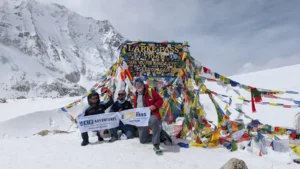 Trekkers posing at Larke Pass (5,106m) during the Manaslu Trek in Nepal, surrounded by snowy mountains and colorful prayer flags.