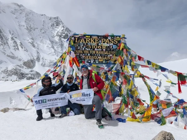 Trekkers posing at Larke Pass (5,106m) during the Manaslu Trek in Nepal, surrounded by snowy mountains and colorful prayer flags.